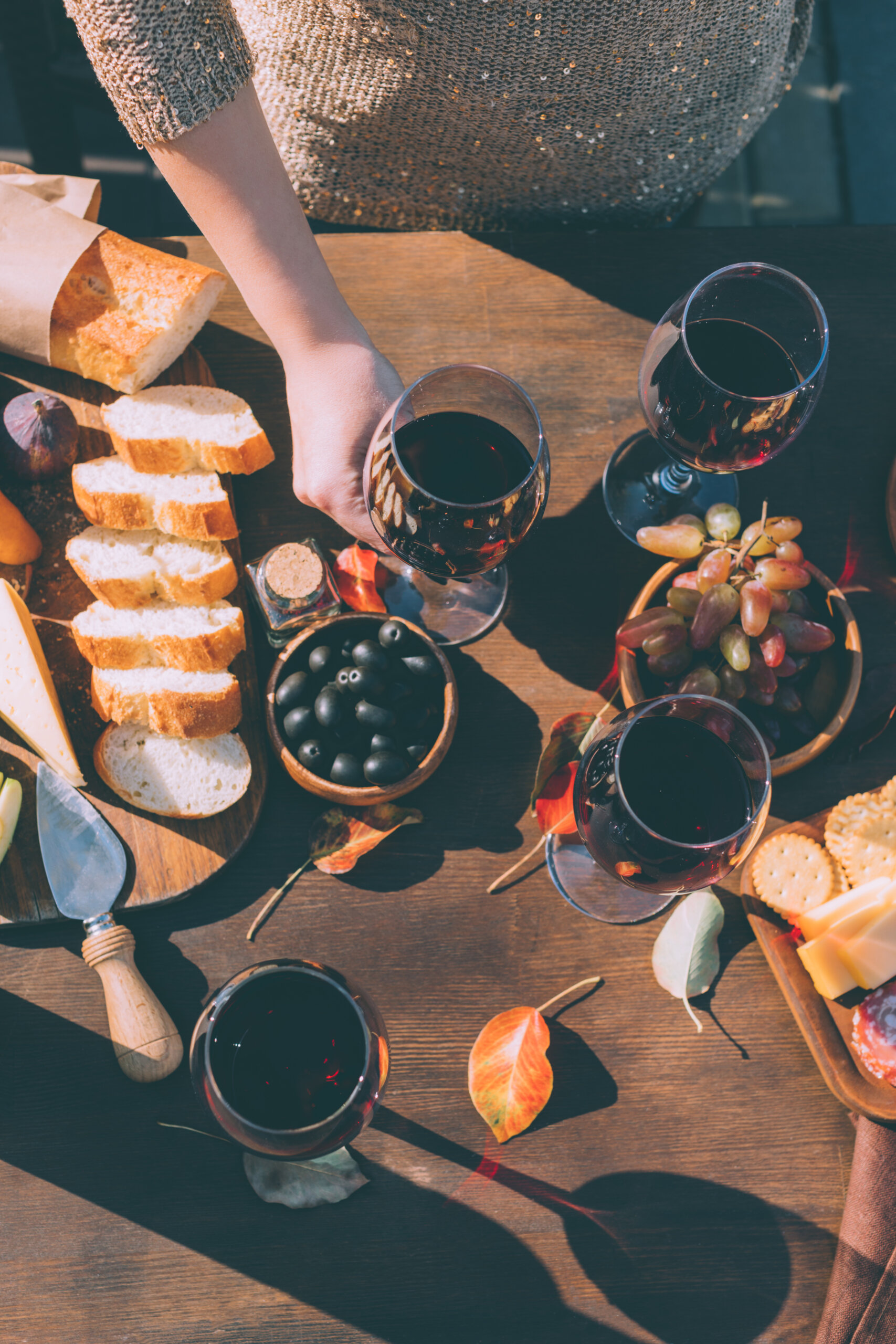 cropped shot of woman holding glass of wine on table full of snacks